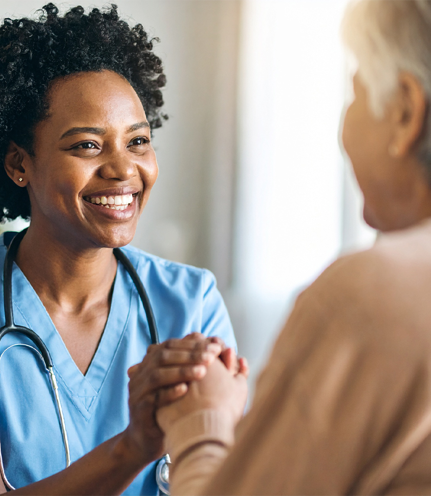 Smiling nurse holding elderly patient's hands in comforting gesture.
