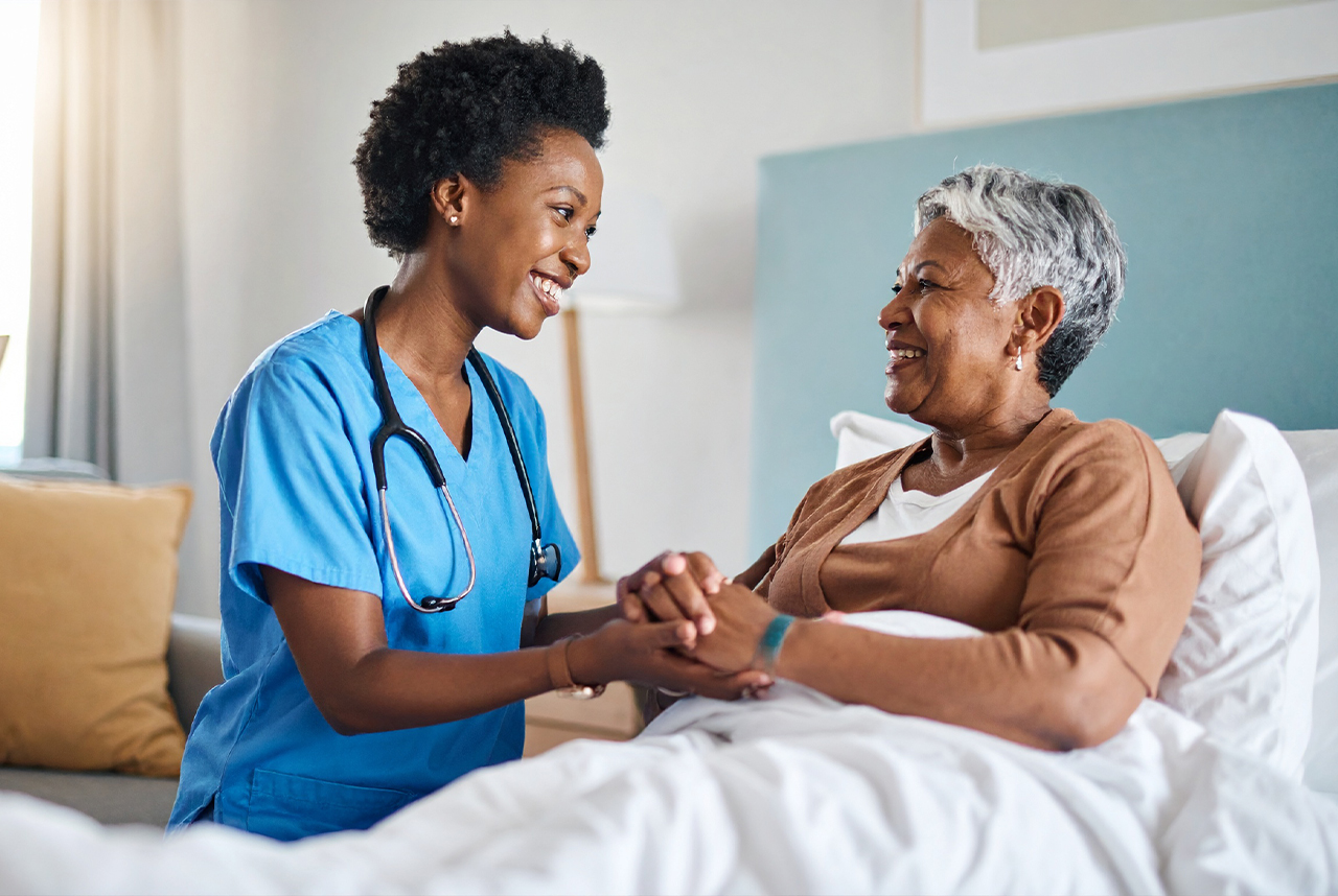 Nurse comforting elderly patient in hospital bed.
